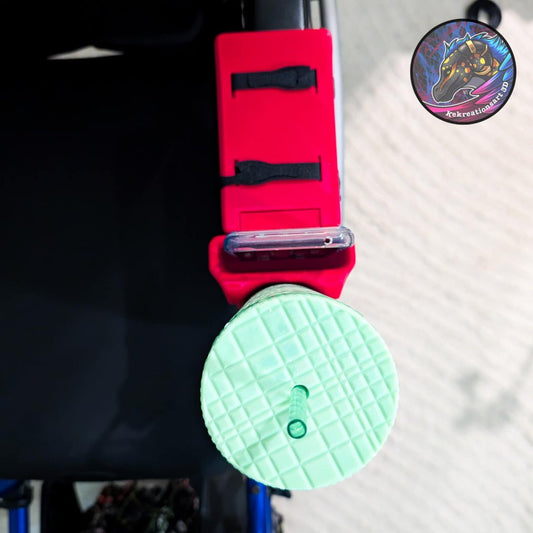 Red wheelchair cup and phone holder attached to a chair, holding a green textured cup and a smartphone.