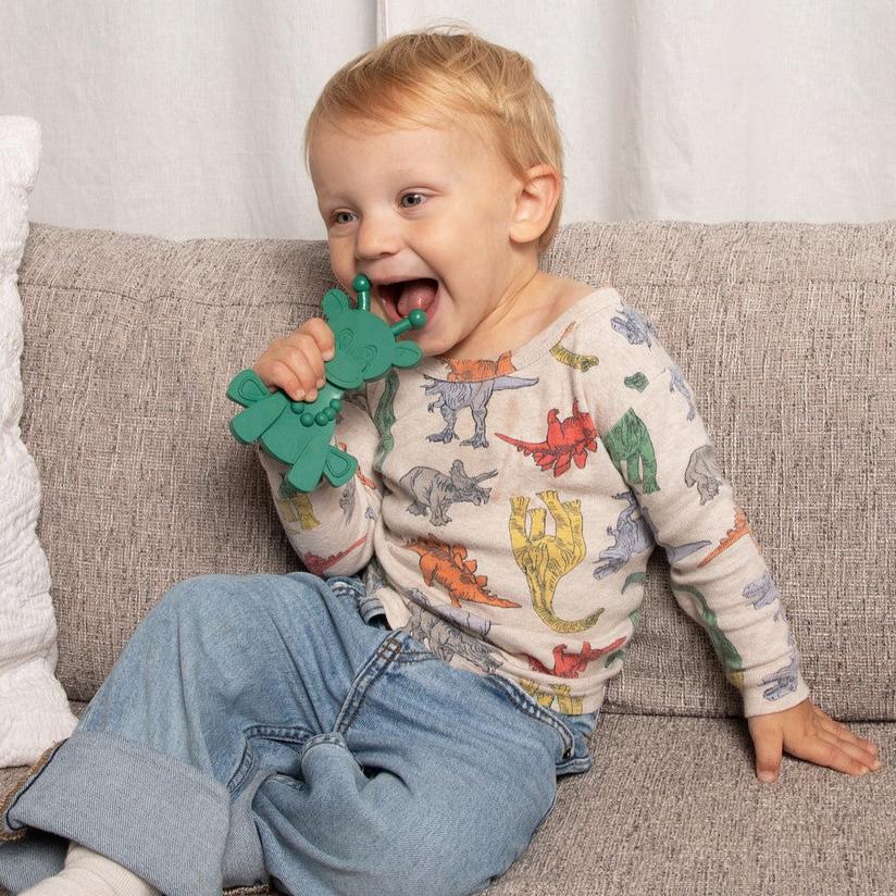 Child sitting on a couch holding a green dinosaur toy