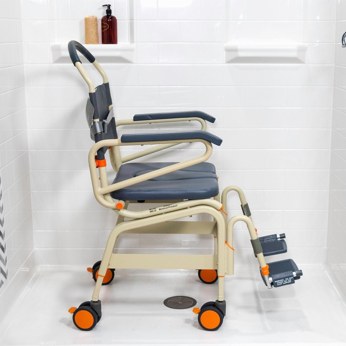 Wide roll-in shower chair front-left view, dark blue seat, back strap, dual foot supports, wheels